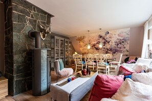 Ein gemütliches Wohnzimmer mit Kamin aus Stein, einem Essbereich mit Stühlen, einem Tisch mit Tablett und einer Wandmalerei mit floralem Muster.