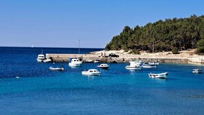 Uma marina costeira com barcos atracados, uma praia arenosa e uma encosta arborizada.