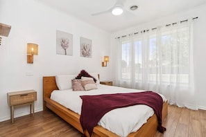 A bedroom with a wooden bed, white walls, and a window with sheer curtains. - Salt & Sand in Seaford (Seaford)