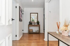 A hallway with a wooden floor, a console table with decorative items, and a mirror on the wall. - Salt & Sand in Seaford (Seaford)