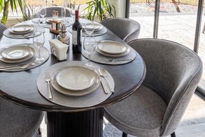 A dining table set for four with plates, cutlery, and a bottle of wine, surrounded by chairs. - Skummeslöv Family Hosue (Skummesloevsstrand)