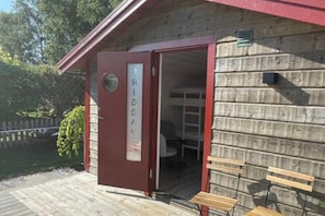 A wooden cabin with a red door, a small porch, and two wooden benches outside. - Skummesloev Family Escape L (Skummesloevsstrand)