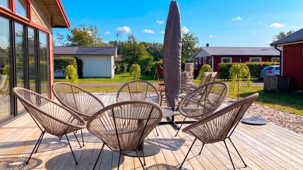 A deck with wicker chairs and a table, overlooking a residential area with houses and greenery. - Skummeslöv Family Hosue (Skummesloevsstrand)