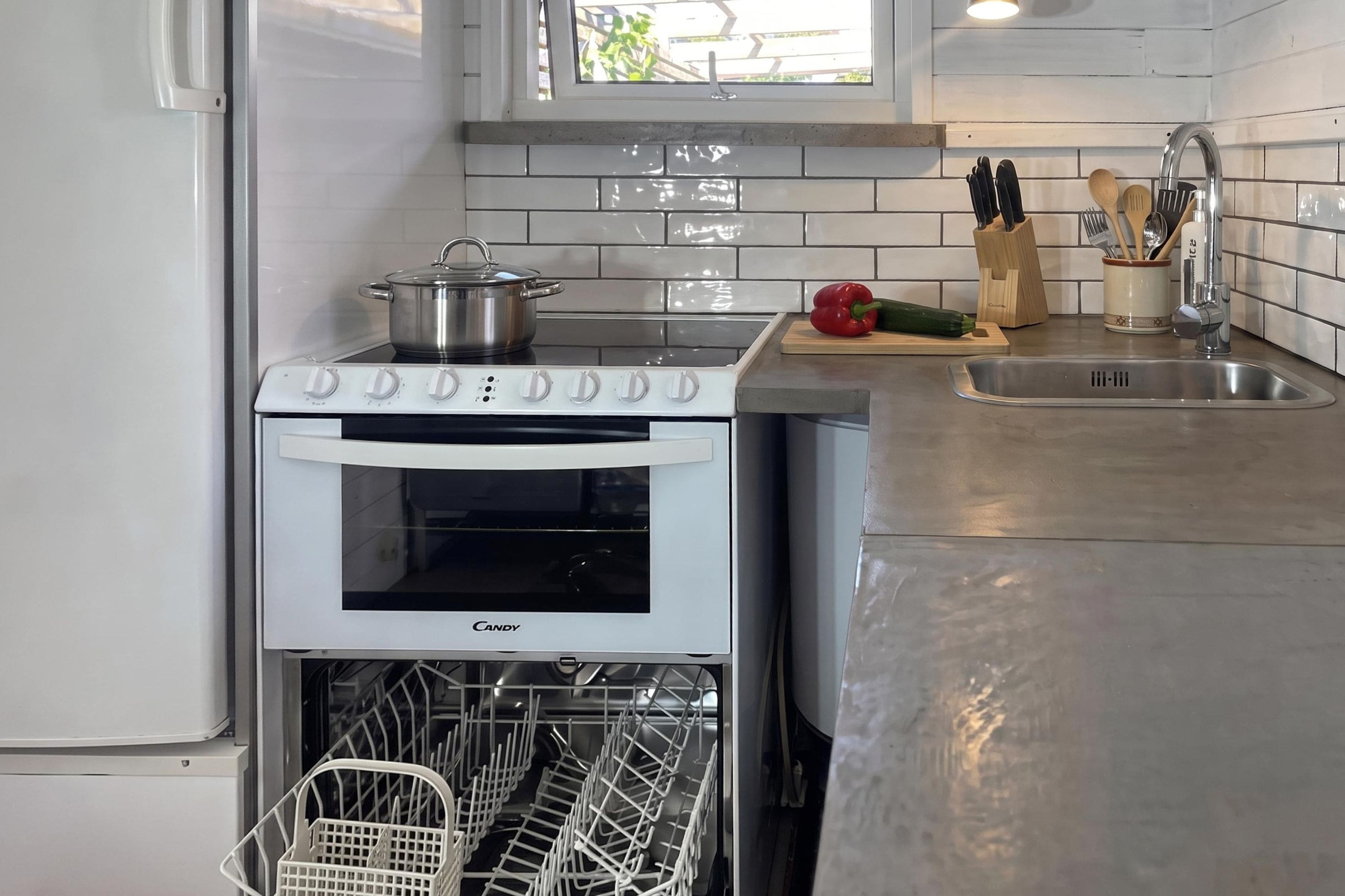 Een kleine keuken met een inbouwoven, een vaatwasser en een roestvrijstalen spoelbak.