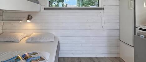A compact room with a bunk bed, a small window, a kitchenette, and a magazine on the bed.