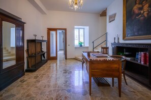Una habitación con suelo de piedra, una mesa de madera, una estantería, una chimenea y un cuadro en la pared.