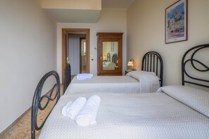 Habitación de hotel con dos camas, una puerta de madera, un cuadro enmarco y una mesita de noche con una lámpara.