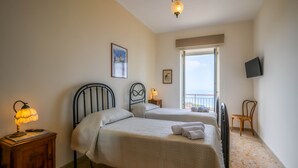 A bedroom with two beds, a nightstand with a lamp, a TV mounted on the wall, and a chair. - Perez Palace, Tucano Room (Belvedere Marittimo)