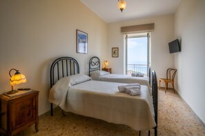 Un dormitorio con dos camas, una mesita de noche con lámpara, un televisor montado en la pared y una silla.