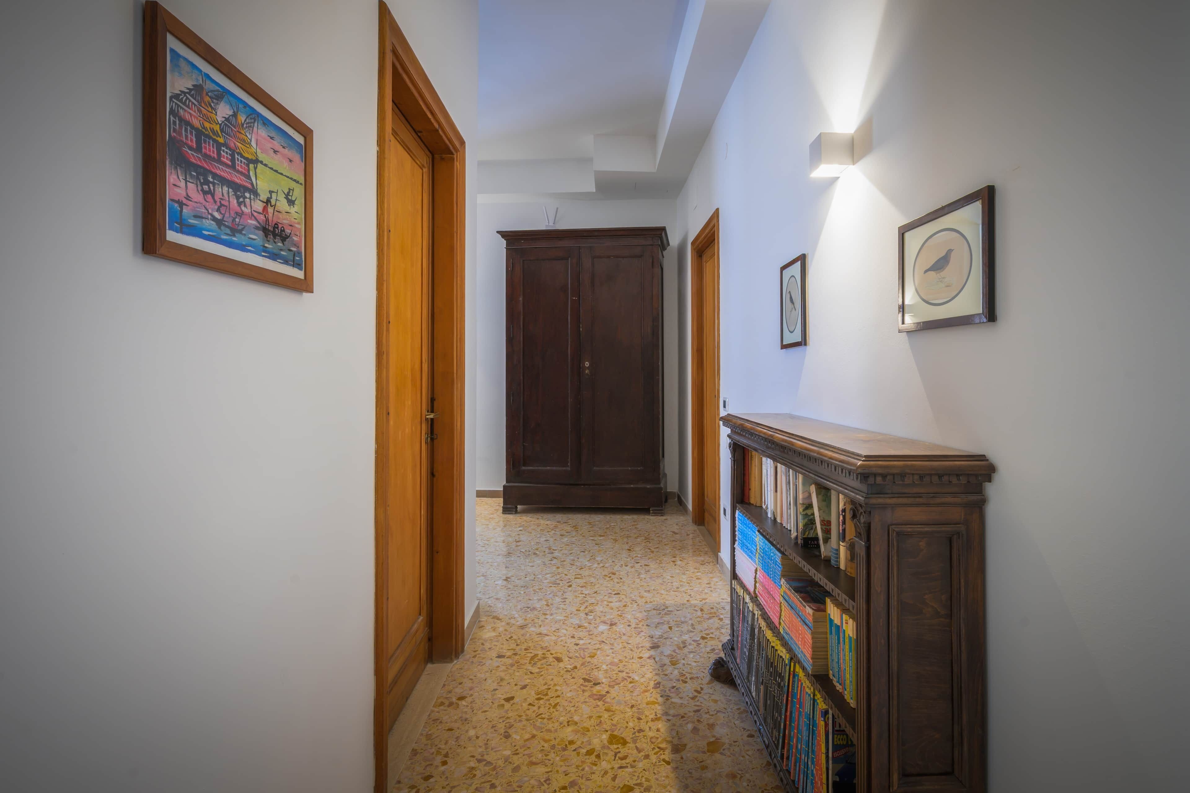 A hallway with a wooden door, a cabinet with books, and a framed picture on the wall.