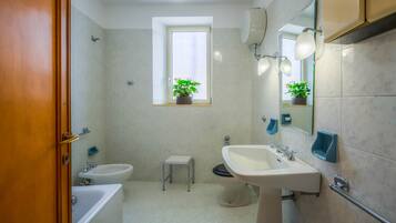A bathroom with a bathtub, a sink, a toilet, a window with a plant, and a mirror.