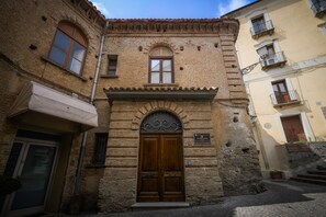 Una calle estrecha con un edificio que presenta una puerta doble de madera, un ventanal pequeño y un frente de piedra.