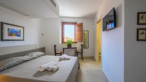 A hotel room with a bed, a desk, a chair, a TV, and a window.