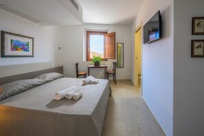 Habitación de hotel con cama, escritorio, silla, televisión y ventana.