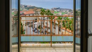 Un balcon avec une balustrade en métal, une vue sur une ville côtière et un ciel dégagé.