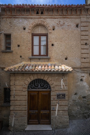 Un edificio in pietra con tetto in tegole, una porta in legno a due battenti e una piccola finestra.