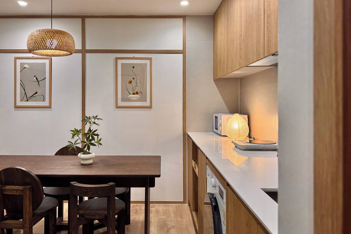 A modern kitchen with wooden cabinets, a dining table with chairs, and two framed artworks on the wall.