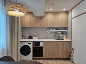Eine moderne Küche mit Holzausstattung, einer Waschmaschine, einer Mikrowelle und einer Pendelleuchte.