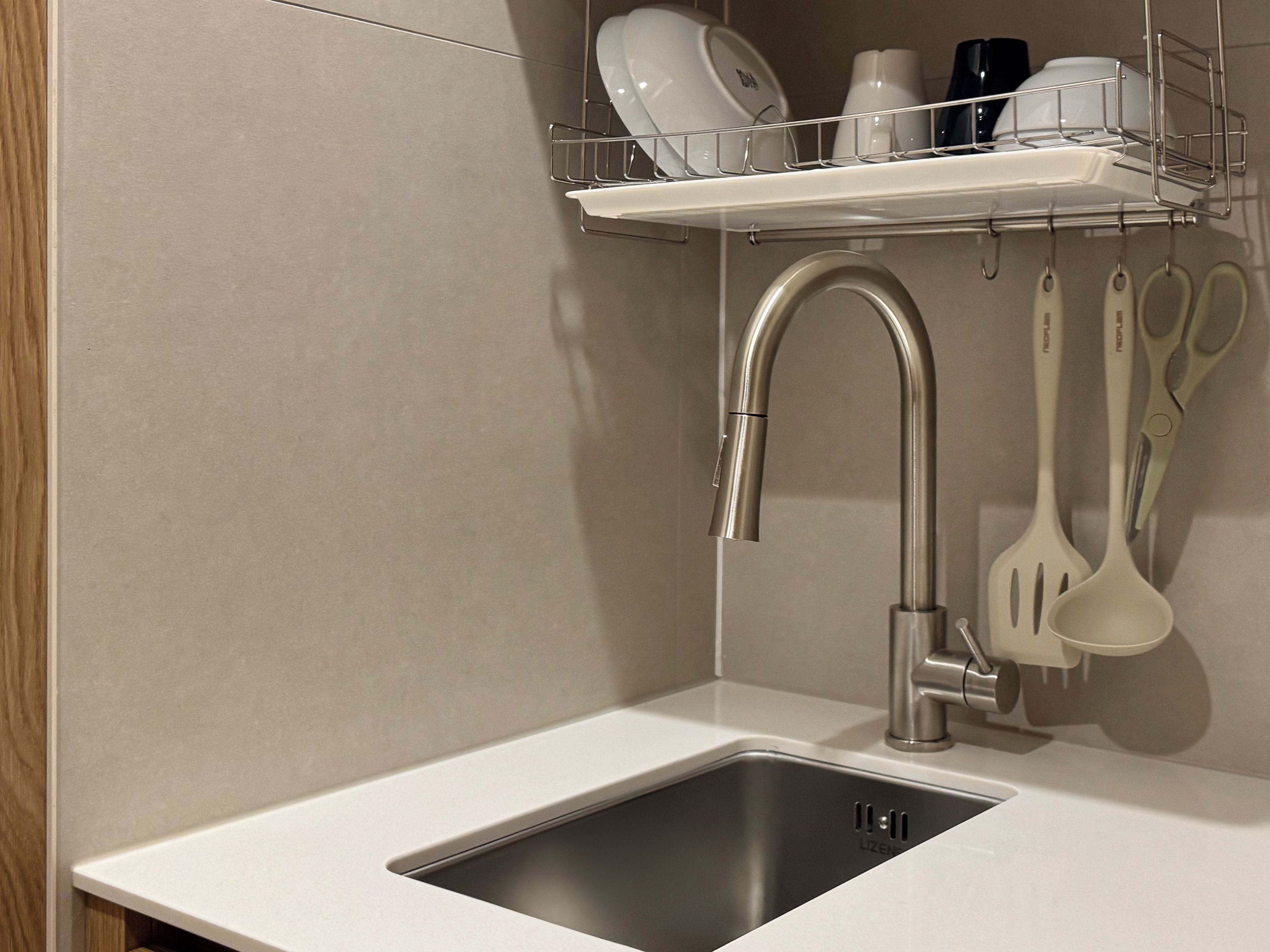 Una cocina con un lavamanos de acero inoxidable, un grifo y un utensilero con espátulas y una cuchara grande.