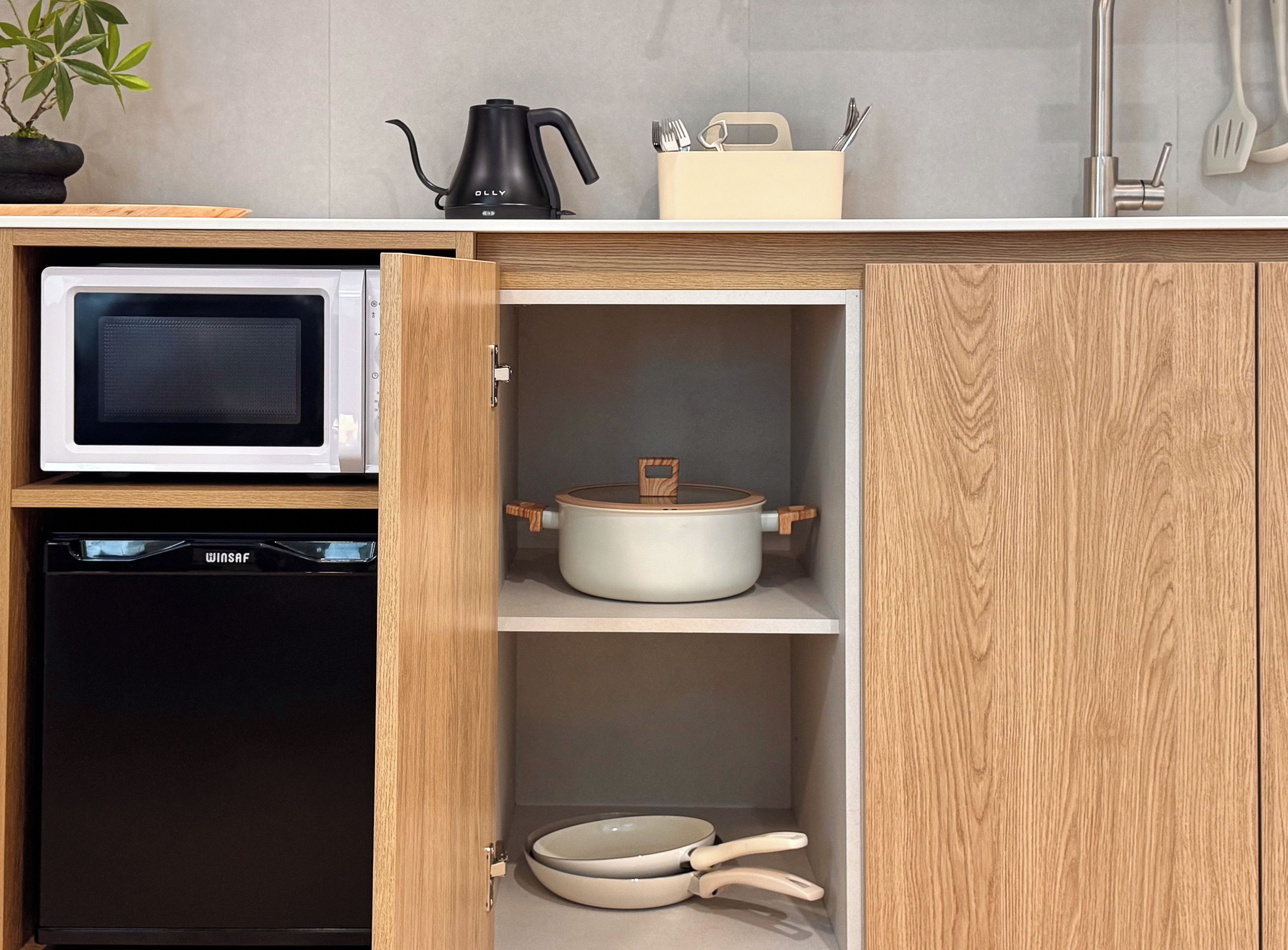 A kitchen with a microwave, a pot, and a set of utensils on the countertop.