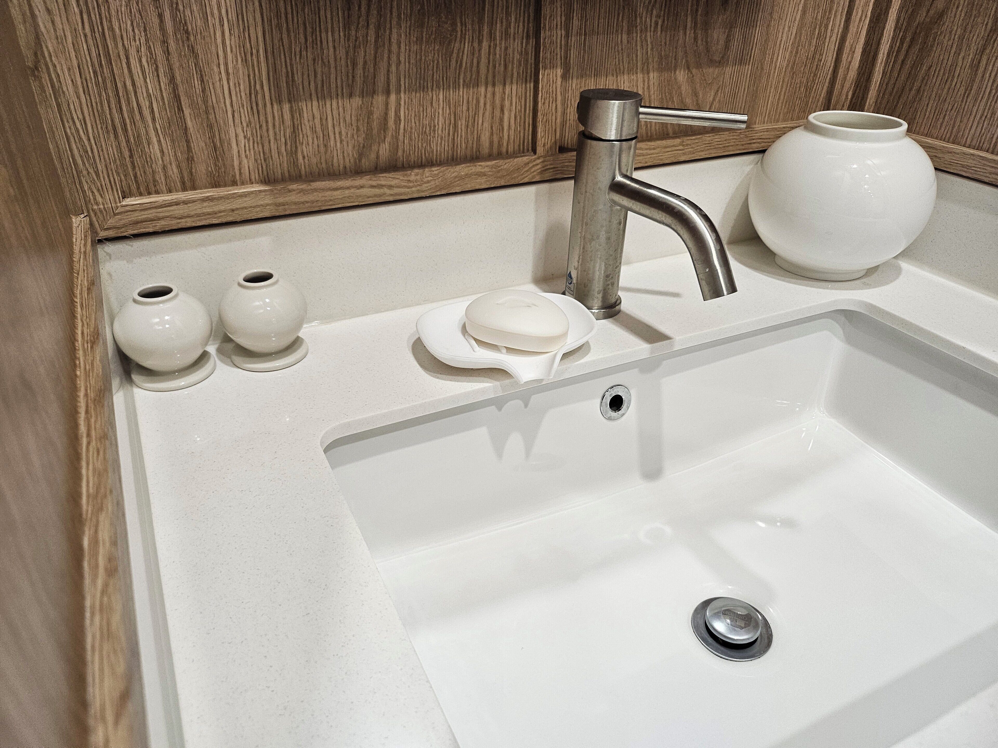 A bathroom sink with a modern faucet, a soap dish, and two small vases.
