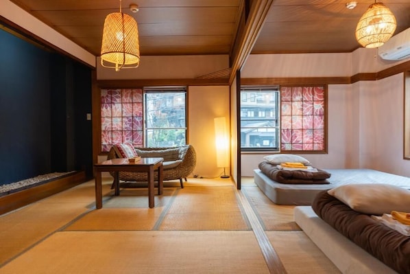 A traditional Japanese-style room with tatami flooring, a low table, a sofa, and a bed.