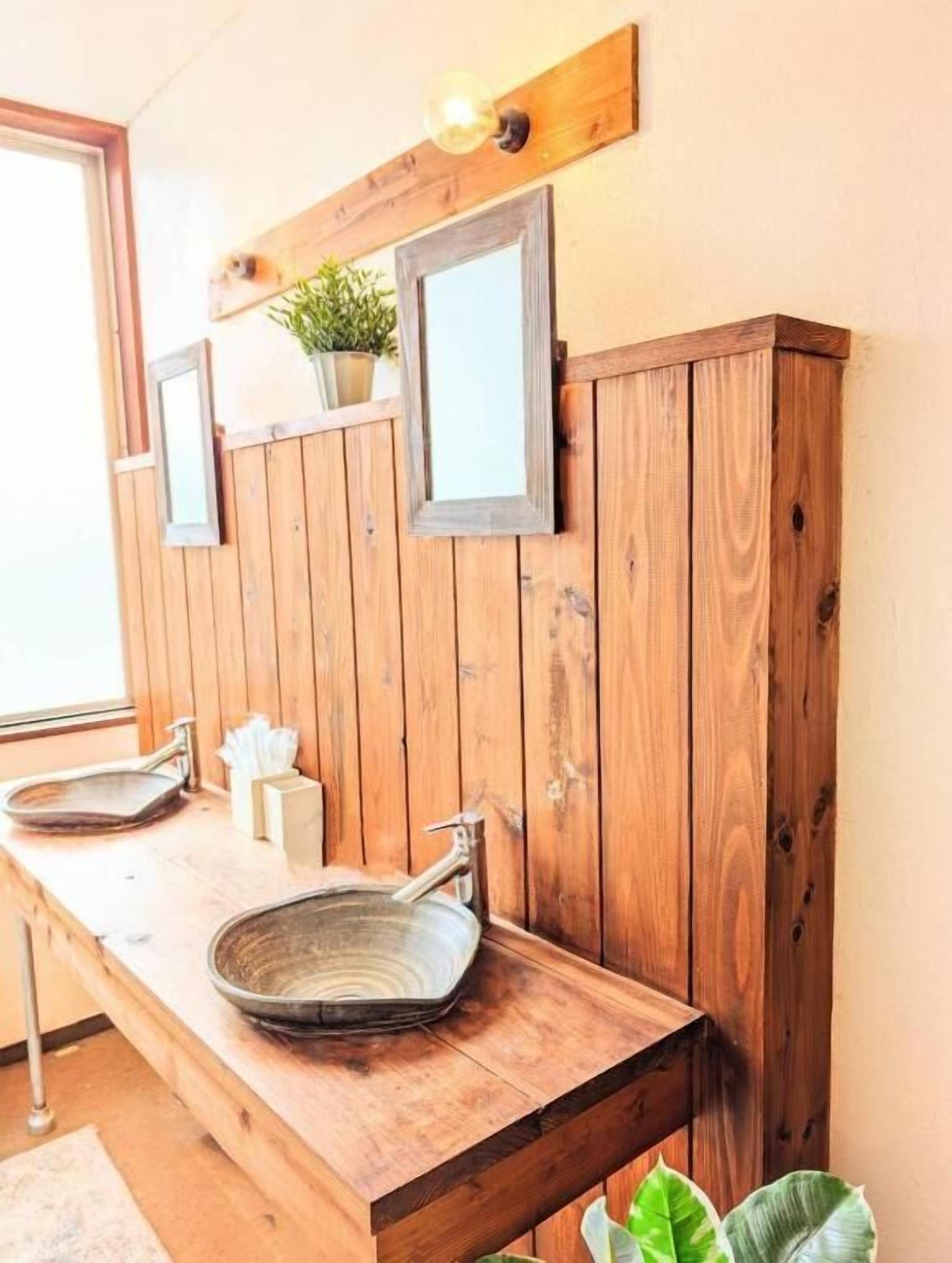 Un mobile bagno in legno con lavabo a bacinella, due specchi e una pianta in vaso.