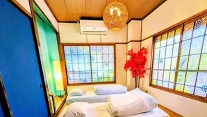 Una habitación tradicional japonesa con suelo de tatami, una cama con ropa blanca, una lámpara colgante y una ventana con vistas.