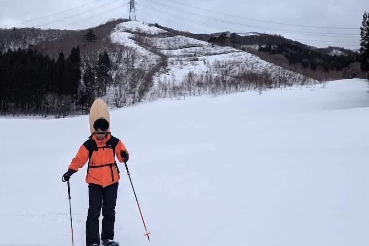 A person skiing on a snowy slope with a power line tower in the background.