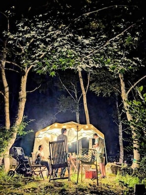A tent with people inside, surrounded by trees.