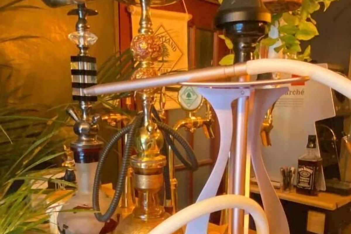 A hookah with a metal base, a glass bowl, and a hose. There are two small metal containers on the table.