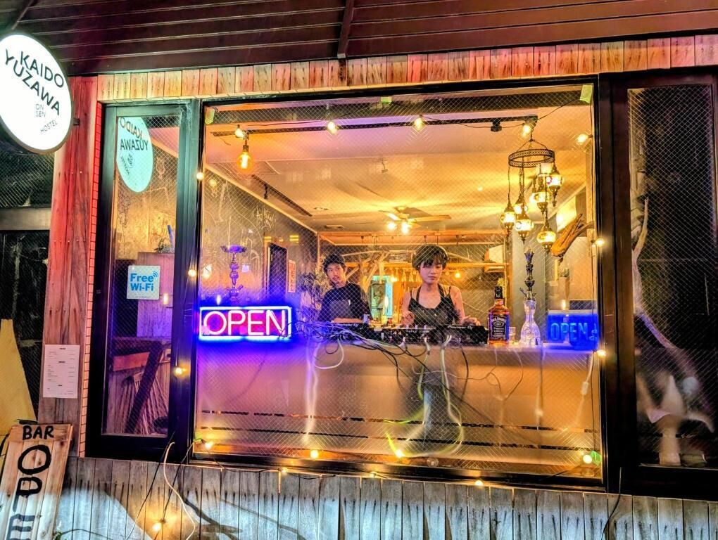 Una zona de bar con un letrero de neón que dice 'OPEN', una cabina de DJ y un cartel que indica 'Free Wi-Fi'.