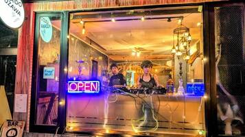 Una zona de bar con un letrero de neón que dice 'OPEN', una cabina de DJ y un cartel que indica 'Free Wi-Fi'.