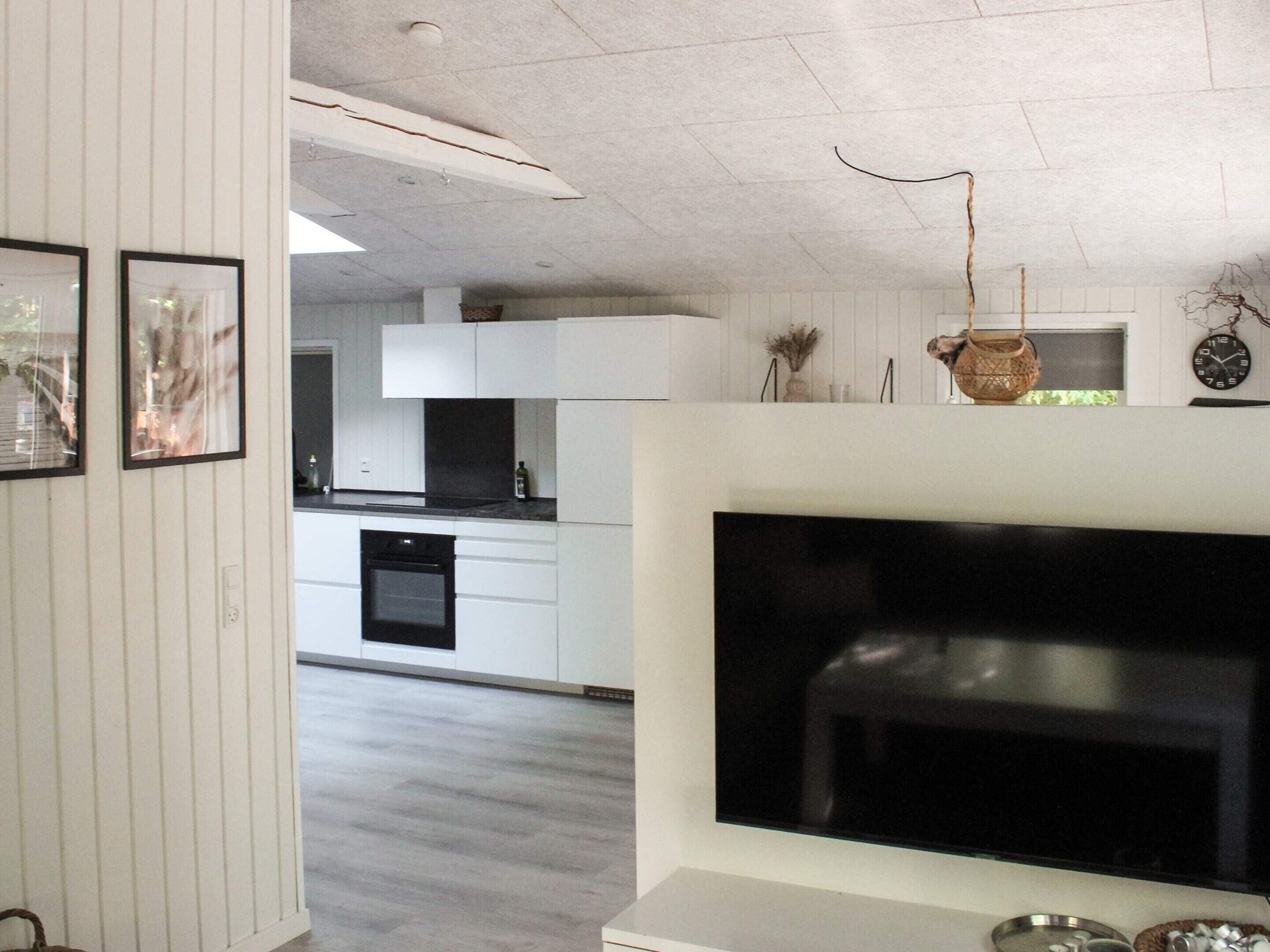A modern living room with a large flat-screen TV, white cabinetry, and a kitchen in the background.