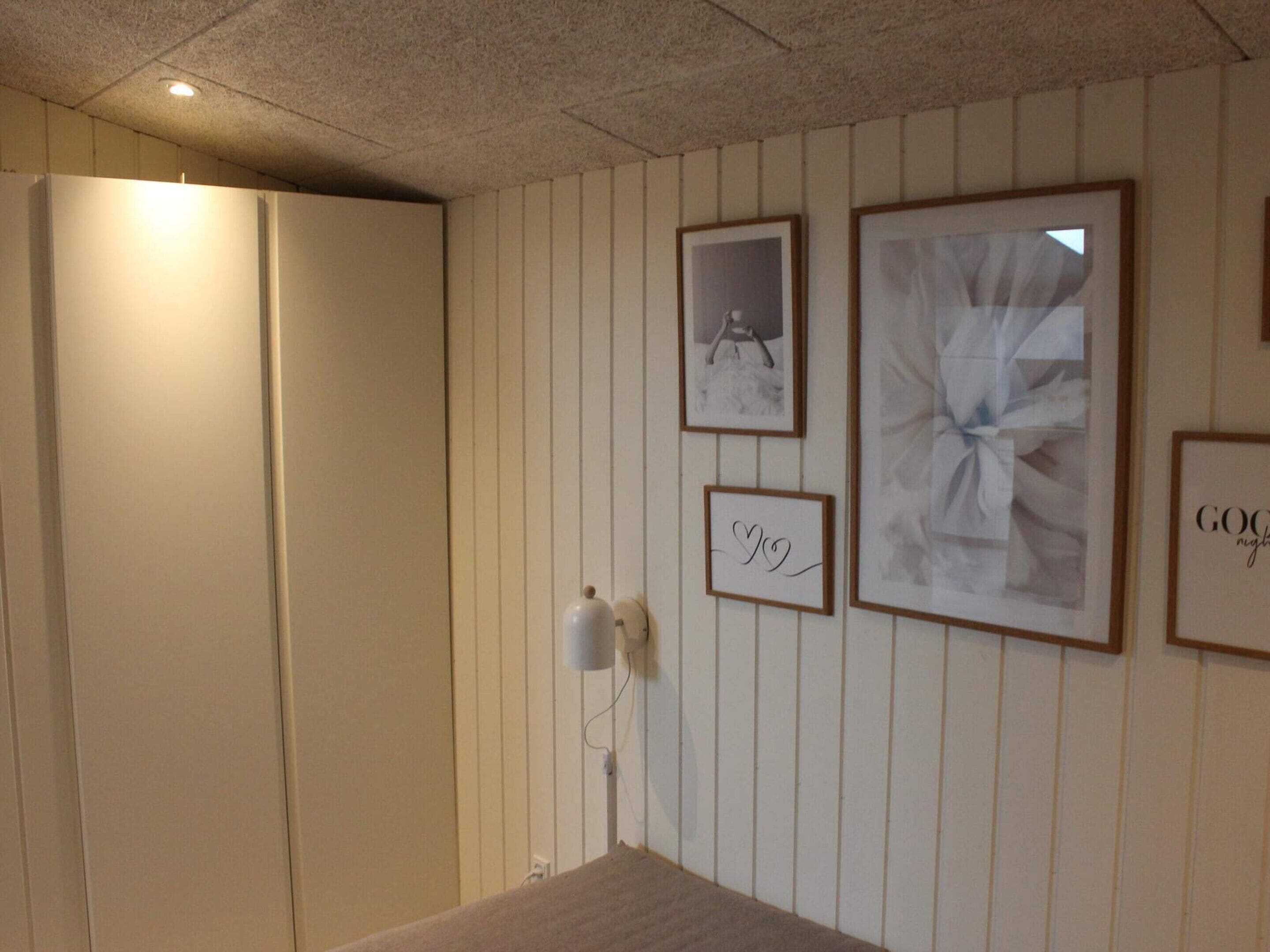 A hotel room with a large wardrobe, a bedside table, and a wall with framed pictures.