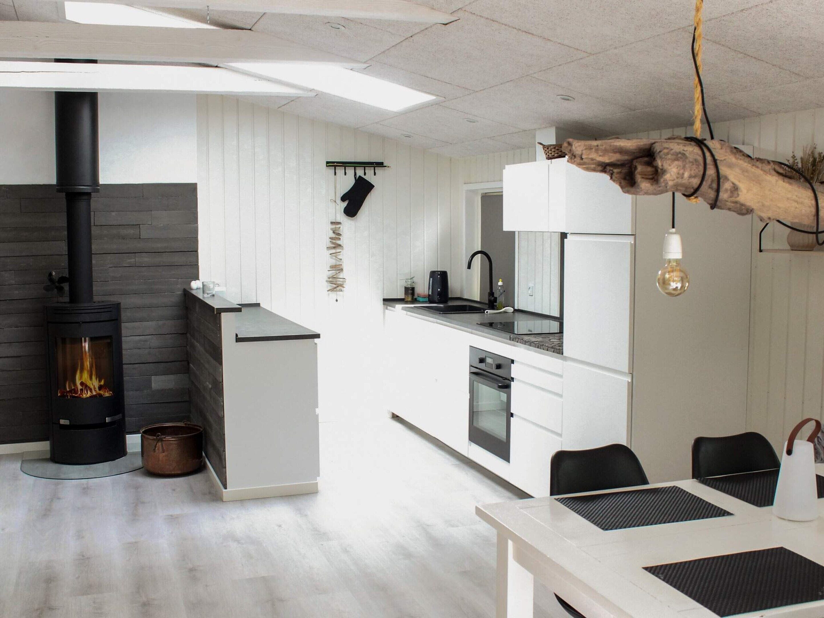 Et moderne køkken med brændeovn, hvide skabe og et spiseområde med bord og stole.