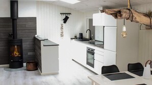 Una cocina moderna con estufa de leña, armarios blancos y un comedor con mesa y sillas.