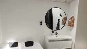 Un baño con una bañera blanca, un espejo redondo, un lavamanos blanco y una puerta con pomo.