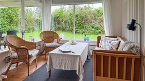 Una habitación acogedora con muebles de mimbre, una mesa con mantel blanco y vistas al exterior con vegetación.