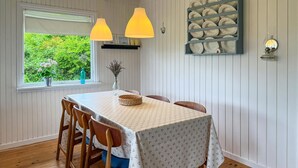 Un comedor con una mesa dispuesta para cuatro, sillas de madera, una ventana con plantas y un aparador de pared.