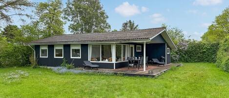 Ein Haus mit überdachter Veranda, Essbereich und Garten.