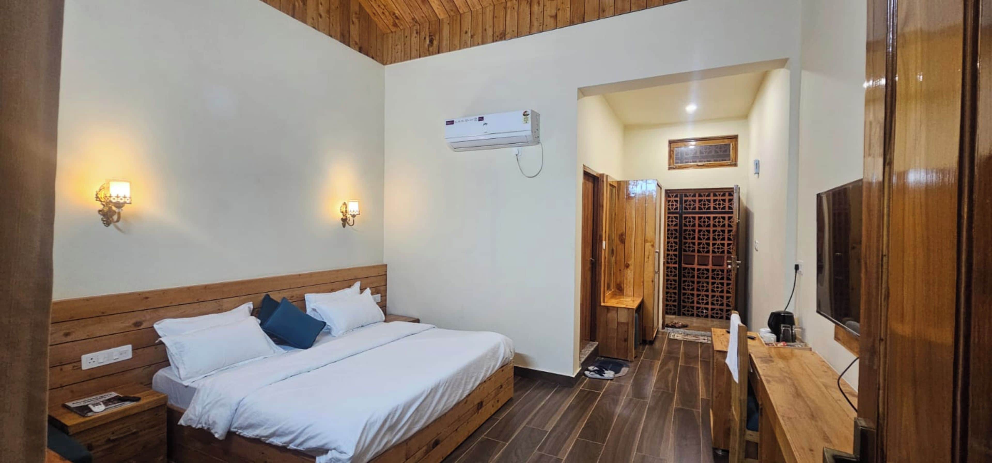 A hotel room with a wooden bed, two wall-mounted lights, a ceiling fan, and a wooden wardrobe.