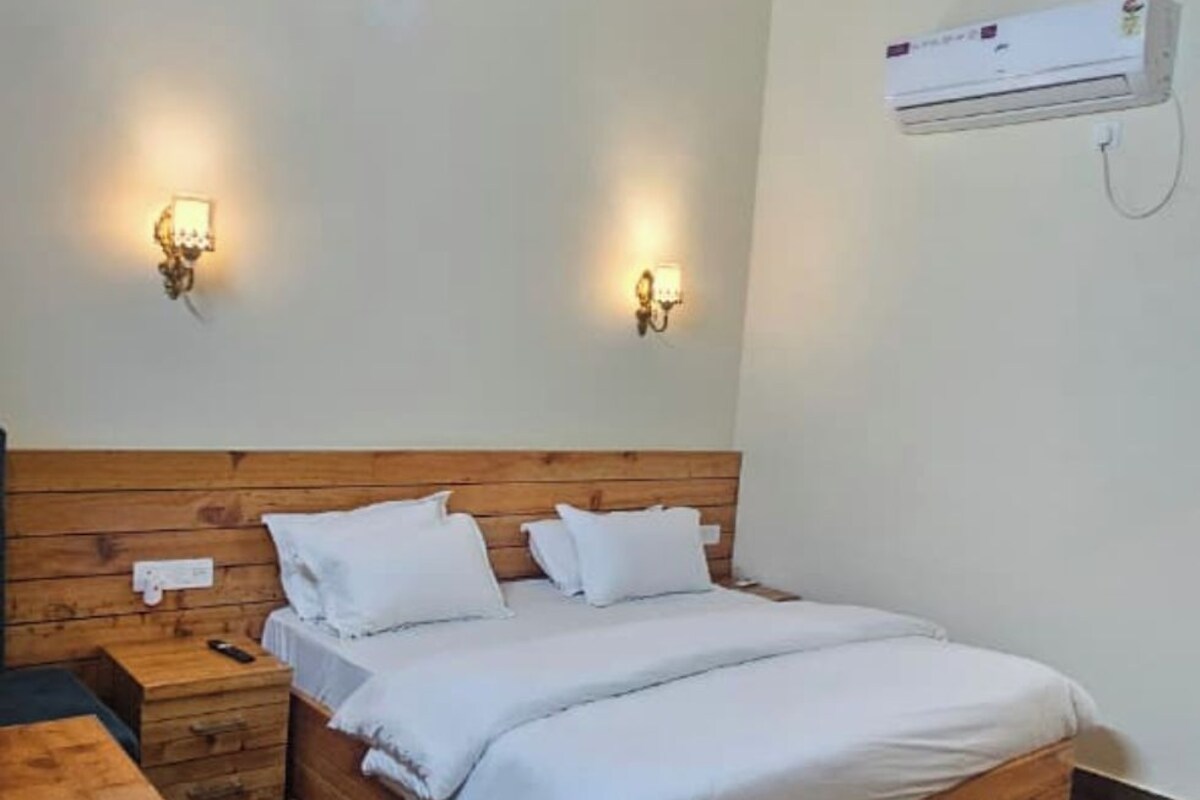 A bedroom with a wooden ceiling, a bed with white bedding, two bedside tables, and an air conditioning unit on the wall.