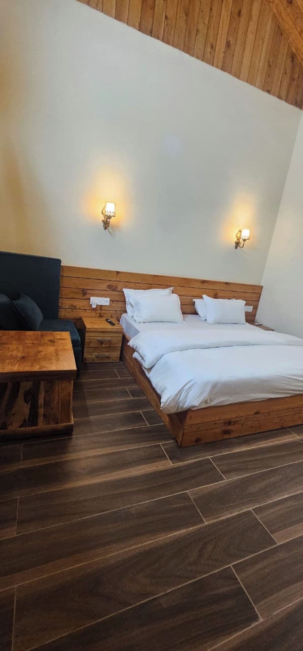 Een kamer met een houten bed, twee nachtkastjes, een bankje en een wandlamp.