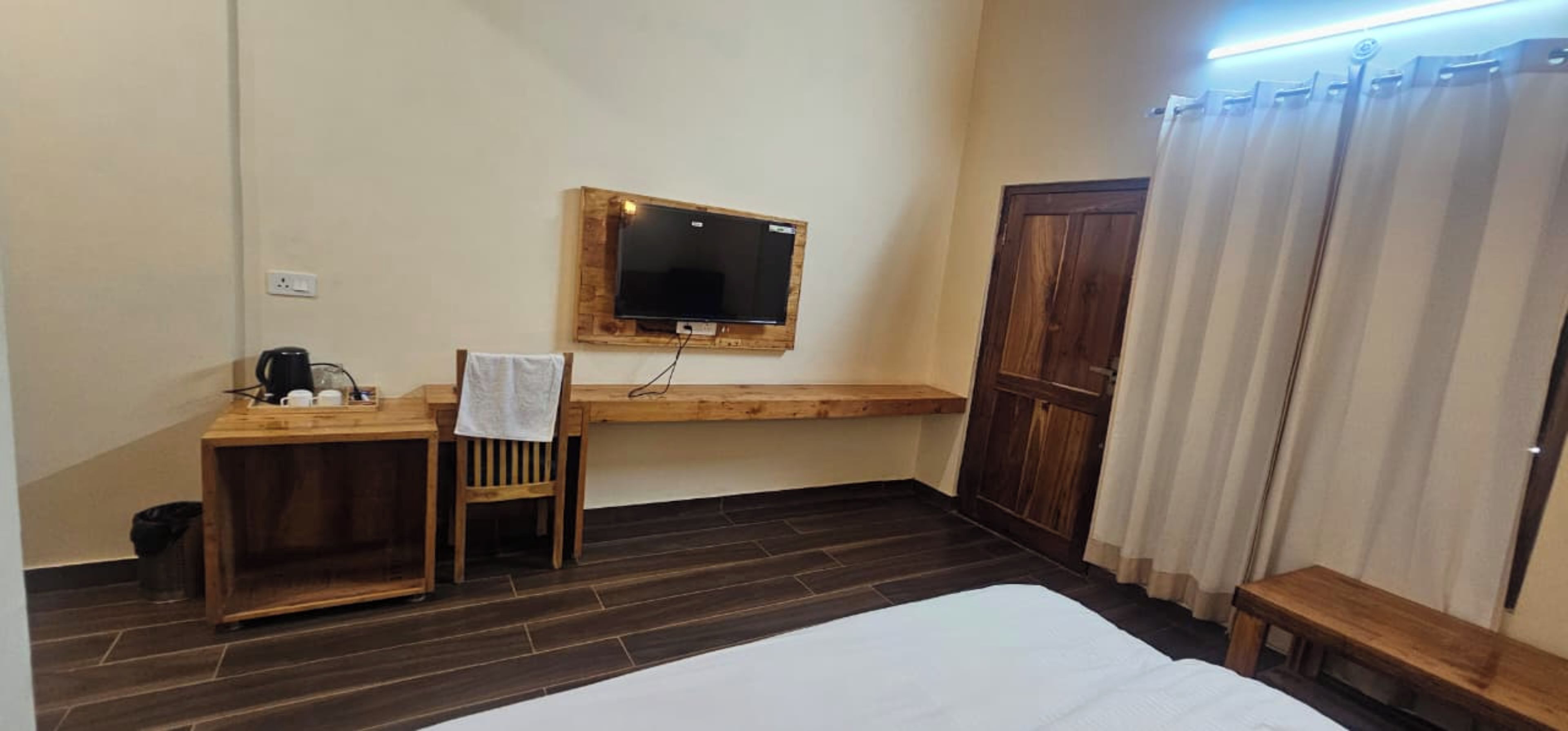 Une chambre d’hôtel avec un lit, un bureau en bois, un téléviseur fixé au mur et une fenêtre avec des rideaux.