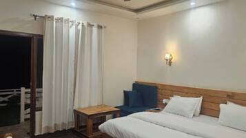 A hotel room with a bed, a chair, a small table, a curtain, and a wall-mounted light fixture.