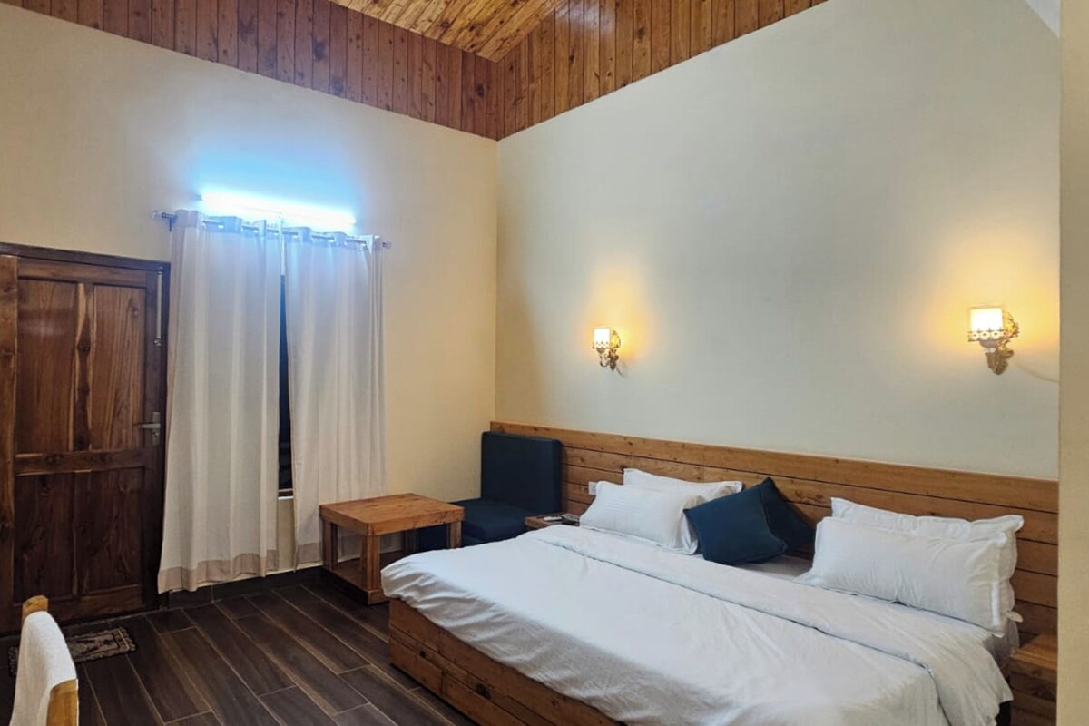 A bedroom with a wooden ceiling, a bed with white bedding, a nightstand, a chair, and a television.