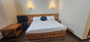 Habitación individual con cama y cabecera de madera, dos mesitas de noche, un banco y dos luces fijadas a la pared.