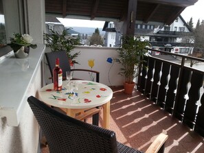 A balcony with a table, chairs, a potted plant, and a bottle of wine. - Vacation apartment Anna (Winterberg)