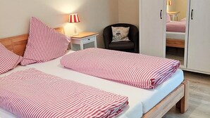 Ett sovrum med en säng, sängbord, en lampa, en stol, en garderob och en randig taklampa.